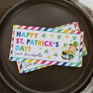 May include: A colorful rainbow striped chocolate bar wrapper with the text "Happy St. Patrick's Day! Love Annabelle". The wrapper features a cartoon leprechaun holding a pot of gold.