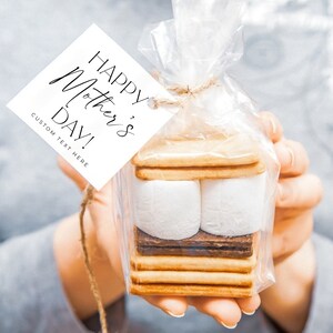 May include: A clear plastic bag filled with a s'mores kit. The kit includes graham crackers, chocolate squares, and marshmallows. A white gift tag with black text reads "Happy Mother's Day! Custom Text Here".