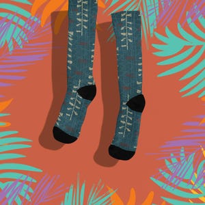 May include: A pair of teal socks with a white and brown pattern, black heels and toes. The socks are set against a coral background with colorful tropical leaf illustrations in orange, teal, and purple.