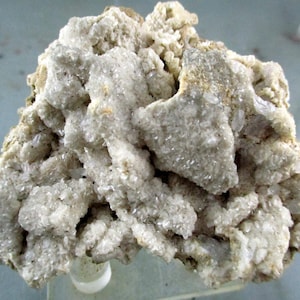 Puede incluir: Primer plano de un espécimen mineral de color claro. La formación rocosa tiene una superficie rugosa y texturizada con estructuras cristalinas. El color es principalmente blanquecino con algunas áreas de color beige y gris. El mineral parece ser cuarzo o un tipo de piedra similar.