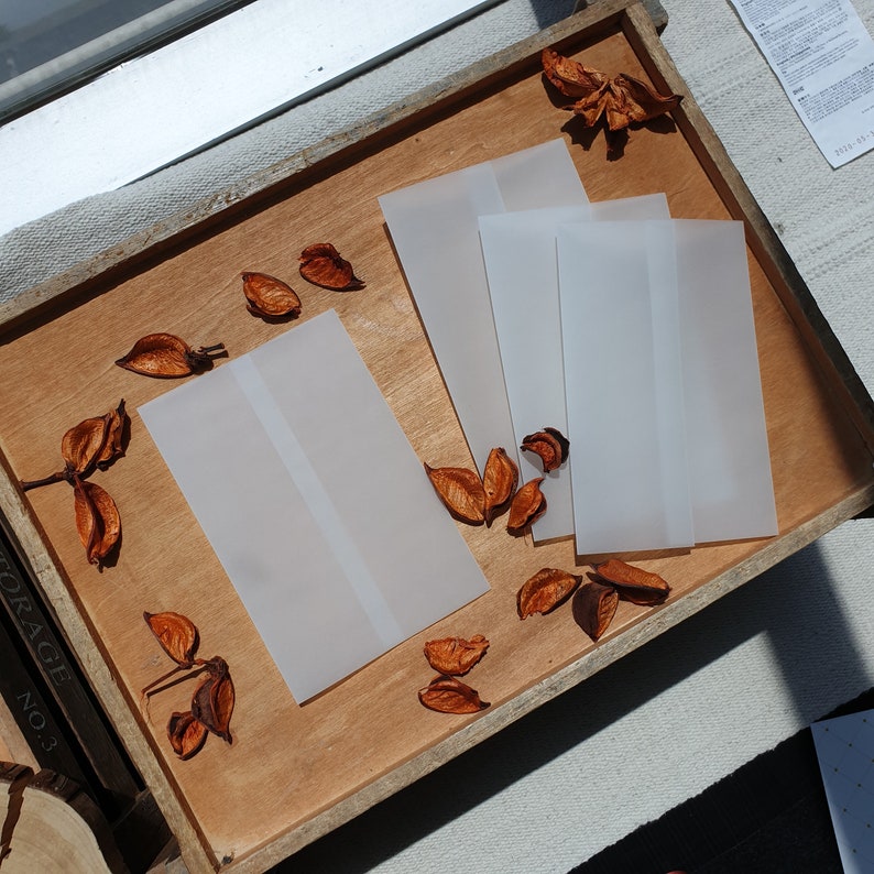 May include: A wooden tray with four white envelopes and dried orange leaves. The envelopes are stacked on top of each other.