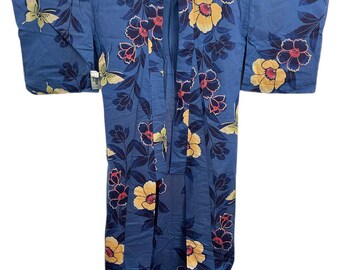 Puede incluir: Un kimono azul con un estampado floral y de mariposas. El kimono presenta flores amarillas y rojas con hojas azul oscuro. También hay mariposas en el diseño. La prenda está colgada de una percha de madera.