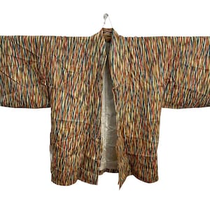 May include: A vintage kimono with a colorful striped pattern in shades of brown, orange, green, and blue. The kimono is open in the front and has wide sleeves. It is hanging from a hanger against a white background.