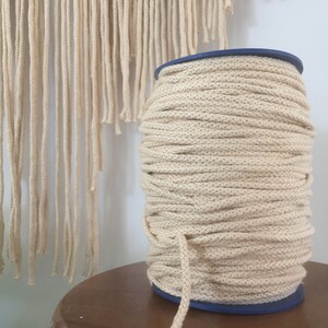 May include: A spool of natural coloured cotton rope, wound tightly around a blue plastic spool. The rope is thick and textured, and is perfect for crafting projects.