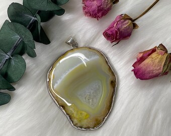May include: A silver pendant featuring a large, natural agate stone with a yellow and white pattern. The stone is set in a silver bezel and has a smooth, polished finish.