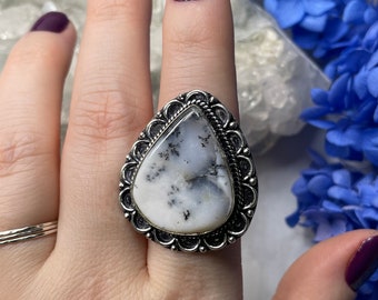 May include: A silver ring with a white and gray teardrop-shaped stone set in a decorative silver bezel.