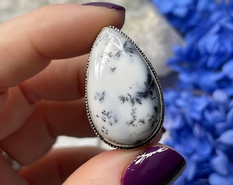 May include: A white and black dendritic agate ring with a silver setting. The ring is in the shape of a teardrop.