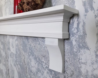 Puede incluir: Estante de madera blanca con un borde decorativo y un soporte lateral. Una botella de vidrio roja y un trozo de madera a la deriva están en el estante.