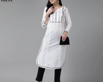 Può includere: Kurta bianco a maniche lunghe in cotone con ricami neri e scollo a V. Il kurta ha uno spacco laterale e un orlo curvo. La modella indossa pantaloni neri e scarpe bianche.