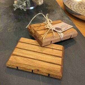 Könnte beinhalten: Zwei Holzseifenhalter mit natürlicher Holzoptik. Die Halter haben Rillen auf der Unterseite, um das Abtropfen von Wasser zu erleichtern. Die Halter sind mit Schnur zusammengebunden und mit einem Etikett versehen, auf dem "Oak Hollow Woodworking, by Tom" steht.