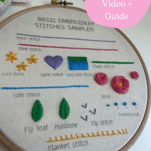 May include: A close-up of an embroidery hoop with a variety of stitches worked in different colors. The stitches include back stitch, stem stitch, lazy daisy, satin stitch, long and short stitch, chain stitch, split stitch, rose, fly stitch, French knot, fly leaf, fishbone, and blanket stitch. The text "PDF pattern + Video + Guide" is in a pink box at the top of the image. The text "BASIC EMBROIDERY STITCHES SAMPLER" is at the top of the hoop.