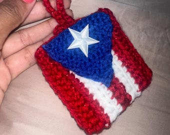 May include: A crocheted ornament in the shape of the Puerto Rican flag. The flag is red, white, and blue with a white star in the blue triangle.