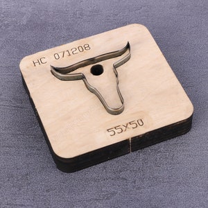 May include: A wooden die-cutting template shaped like a bull's head with horns. The template is labeled "HC 071208" and "55x50".