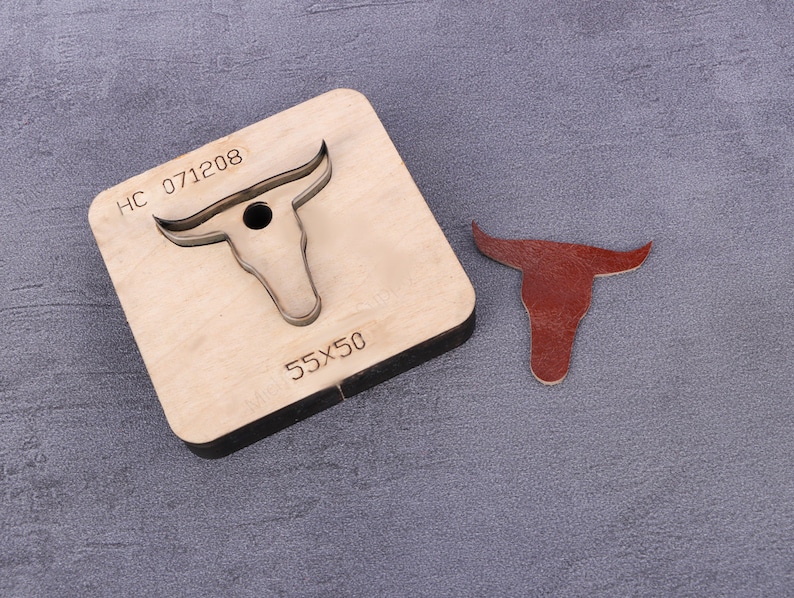 May include: A wooden leather craft punch with a bull's head design. The punch is labeled "HC 071208" and "55X50". A brown leather cutout of a bull's head is shown next to the punch.