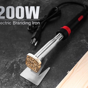 Puede incluir: Un hierro de marcar eléctrico de 200W con mango negro y rojo, eje de metal plateado y cabezal de sello de latón con forma de pan. La herramienta incluye un cable de alimentación negro y descansa sobre un soporte de metal plateado.