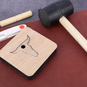 May include: A wooden leather craft punch shaped like a bull's head with a metal cutting die. A rubber mallet and a pair of scissors are also in the image.