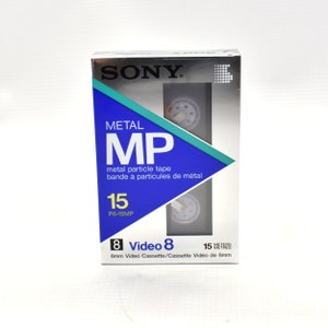 May include: A silver and blue box for a Sony Video 8 cassette tape. The box says "Metal MP" and "metal particle tape" in English and French. The tape is 15 minutes long and is a Video 8 cassette.