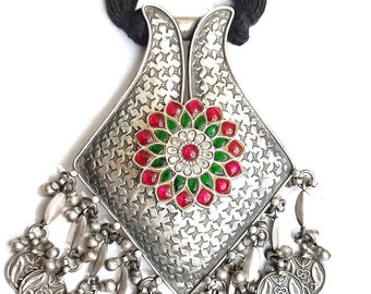 May include: A silver pendant necklace with a square-shaped pendant featuring a red and green floral design. The pendant is adorned with small, round stones and has a textured surface. The necklace has a black cord and is decorated with silver beads and charms.