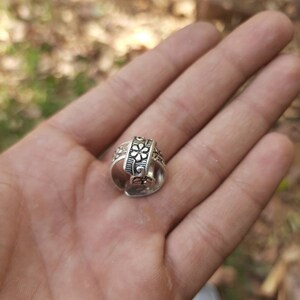 Puede incluir: Un anillo de plata con un diseño floral. El anillo está abierto y tiene una banda decorativa.