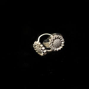 Puede incluir: Un anillo de plata con dos diseños de girasol. El anillo está hecho de metal y tiene un acabado brillante.