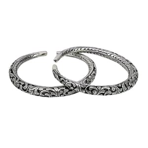 May include: Two silver bangles with intricate floral designs. The bangles are open and have a smooth, polished finish.
