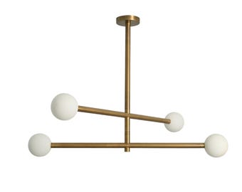 May include: Modern brass chandelier with four white globe lights. The fixture has a minimalist design with a central vertical rod and horizontal arms extending outwards. The light fixtures are ideal for a dining room or living room.