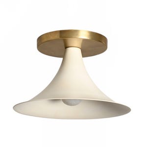May include: Cream-colored ceiling light fixture with a brass-colored circular base. The light has a conical shade and a single bulb. The fixture is designed for ceiling mounting and is suitable for various interior styles.