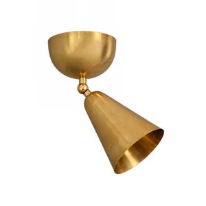 May include: A brass-colored, cone-shaped spotlight fixture. The fixture has a rounded, bowl-shaped base and a cone-shaped light. The light is angled downward, and the fixture is made of a shiny, metallic material.