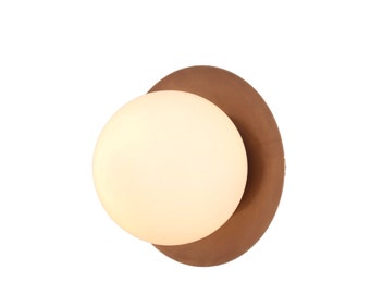 May include: A modern wall sconce featuring a large, round, off-white light fixture set against a circular, brown backing. The sconce has a minimalist design, perfect for contemporary interiors.