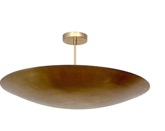 May include: A ceiling light fixture featuring a large, shallow, circular brass-toned metal shade with a brushed finish. The shade is suspended by a thin, vertical brass-toned rod connected to a matching circular canopy mount at the top.