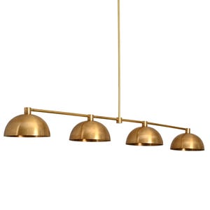May include: A brass four-light linear pendant light fixture with a long, straight bar and four dome-shaped shades.