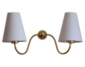May include: A double-light wall sconce with a gold-toned metal frame. The sconce features two white, cone-shaped lampshades. The design is symmetrical, with the shades positioned on either side of a central sphere.