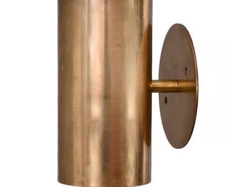 May include: A cylindrical wall sconce made of brushed brass. The sconce features a round backplate and a horizontal arm connecting to the cylindrical light holder. The fixture is designed for wall mounting and has a minimalist, modern aesthetic.