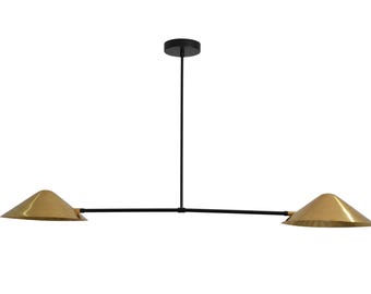 May include: Modern pendant light fixture with two conical brass shades and a black frame. The light hangs from a black rod and a circular ceiling mount. The shades are angled downward.