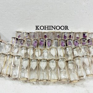 K&ouml;nnte beinhalten: Eine Gruppe von 25 goldgerahmten Sanduhren mit wei&szlig;em Sand. Die Sanduhren sind in durchsichtigem Plastik verpackt und in Reihen angeordnet. Das Wort "KOHINOOR" ist in schwarzen Buchstaben auf wei&szlig;em Hintergrund gedruckt.