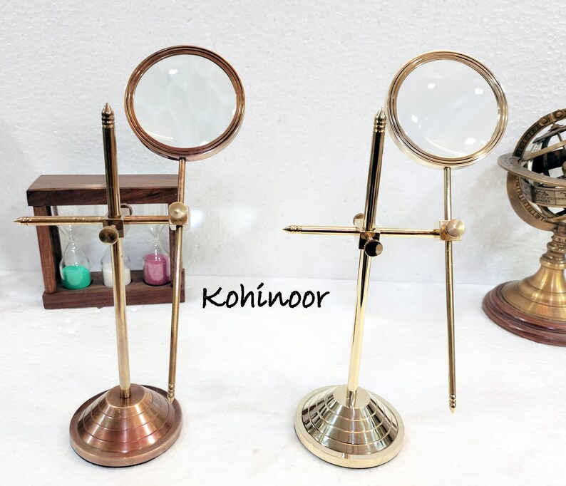 May include: Two brass magnifying glasses on stands. Each stand has a round base and a crossbar with a magnifying glass attached to it. The magnifying glasses are clear and have a brass frame.