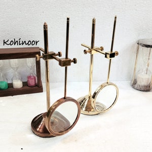 May include: Two antique brass magnifying glass stands with adjustable arms and round magnifying lenses. The stands have a brass base and a gold finish.