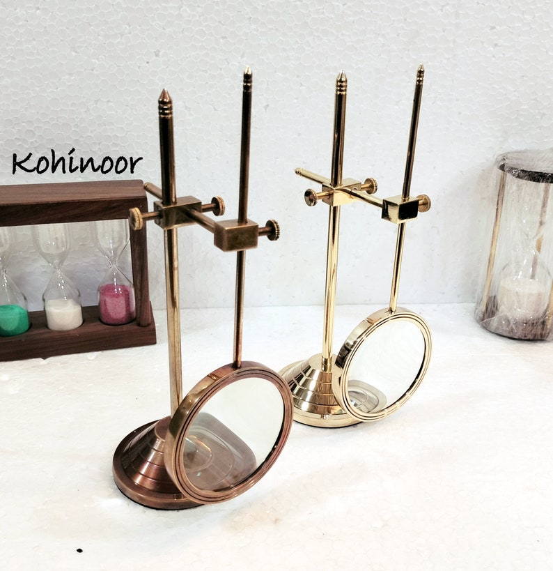 May include: Two antique brass magnifying glass stands with adjustable arms and round magnifying lenses. The stands have a brass base and a gold finish.