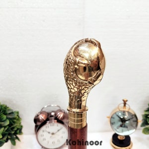 Puede incluir: Un mango de bastón de color dorado con un diseño de serpiente detallado. El mango está hecho de latón y tiene una superficie texturizada.