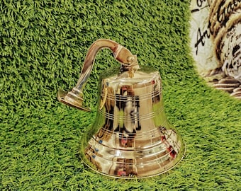 Könnte beinhalten: Eine polierte Messingglocke mit einer Aufhängeschlaufe. Die Glocke hat eine abgerundete Form und eine glatte, glänzende Oberfläche.