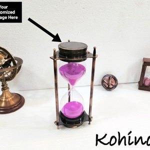 Peut inclure: Un sablier en laiton avec un sablier de sable rose. Le sablier est sur une surface blanche avec une boussole et un petit globe en arrière-plan. Le haut du sablier a un espace pour un message personnalisé.