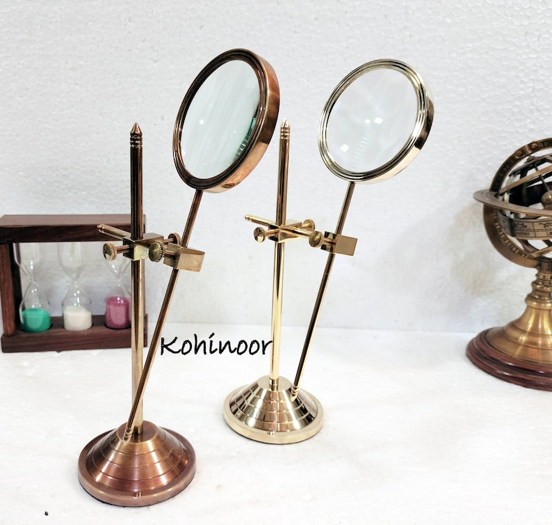 May include: Two brass magnifying glasses on stands. The magnifying glasses have round lenses and are mounted on adjustable arms. The stands have a round base and a vertical rod. The stands are made of brass and have a polished finish.