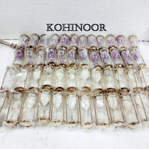 K&ouml;nnte beinhalten: Eine Gruppe von 40 goldfarbenen Sanduhren mit klaren Glaskolben. Die Sanduhren sind in Reihen auf einer wei&szlig;en Oberfl&auml;che angeordnet. Das Wort "KOHINOOR" ist in schwarzen Buchstaben auf wei&szlig;em Hintergrund &uuml;ber den Sanduhren gedruckt.
