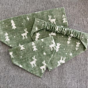 May include: A set of green fabric accessories with a white Christmas tree and reindeer pattern. The set includes a headband and two bandanas, perfect for pets or matching outfits. The fabric has a textured appearance.