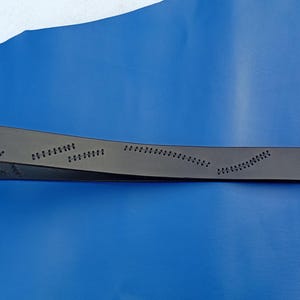 May include: A black leather belt with decorative stitching and a silver-colored buckle. The belt has a series of small, evenly spaced perforations along its length, creating a unique design. The belt is displayed against a blue background.