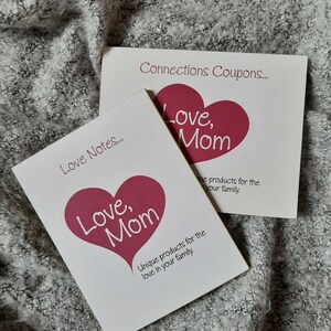 May include: Two white cards with pink hearts and the text "Love, Mom" on them. The cards are titled "Love Notes..." and "Connections Coupons..." and both say "Unique products for the love in your family."