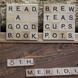 May include: A close-up of a wooden board with letter tiles spelling out the words "BREW", "SIP", "LOVE", "TEAS", "READ", "A", "GOOD", "BOOK", "BREW", "TEAS", "CUPS", "POTS", "TEAS", "ICED", "LEAF", "MINT", "5TH", and "MERIDIAN".
