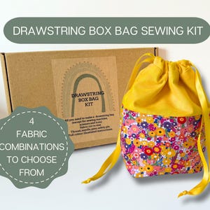 May include: A sewing kit for a drawstring box bag. The kit includes a yellow drawstring bag with a floral pattern on the bottom, a cardboard box, and the text "DRAWSTRING BOX BAG SEWING KIT". The image also includes the text "4 FABRIC COMBINATIONS TO CHOOSE FROM".