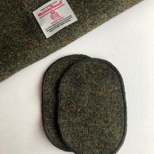 Puede incluir: Dos parches ovalados de tela de tweed verde con costuras negras alrededor de los bordes. Los parches están hechos de Harris Tweed, un tipo de tela de lana de las Hébridas Exteriores de Escocia.