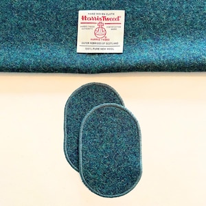 Puede incluir: Dos parches ovalados de tela Harris Tweed de color verde azulado oscuro. La tela está tejida con un sutil patrón verde y azul. Los parches están bordeados con una costura azul oscuro.